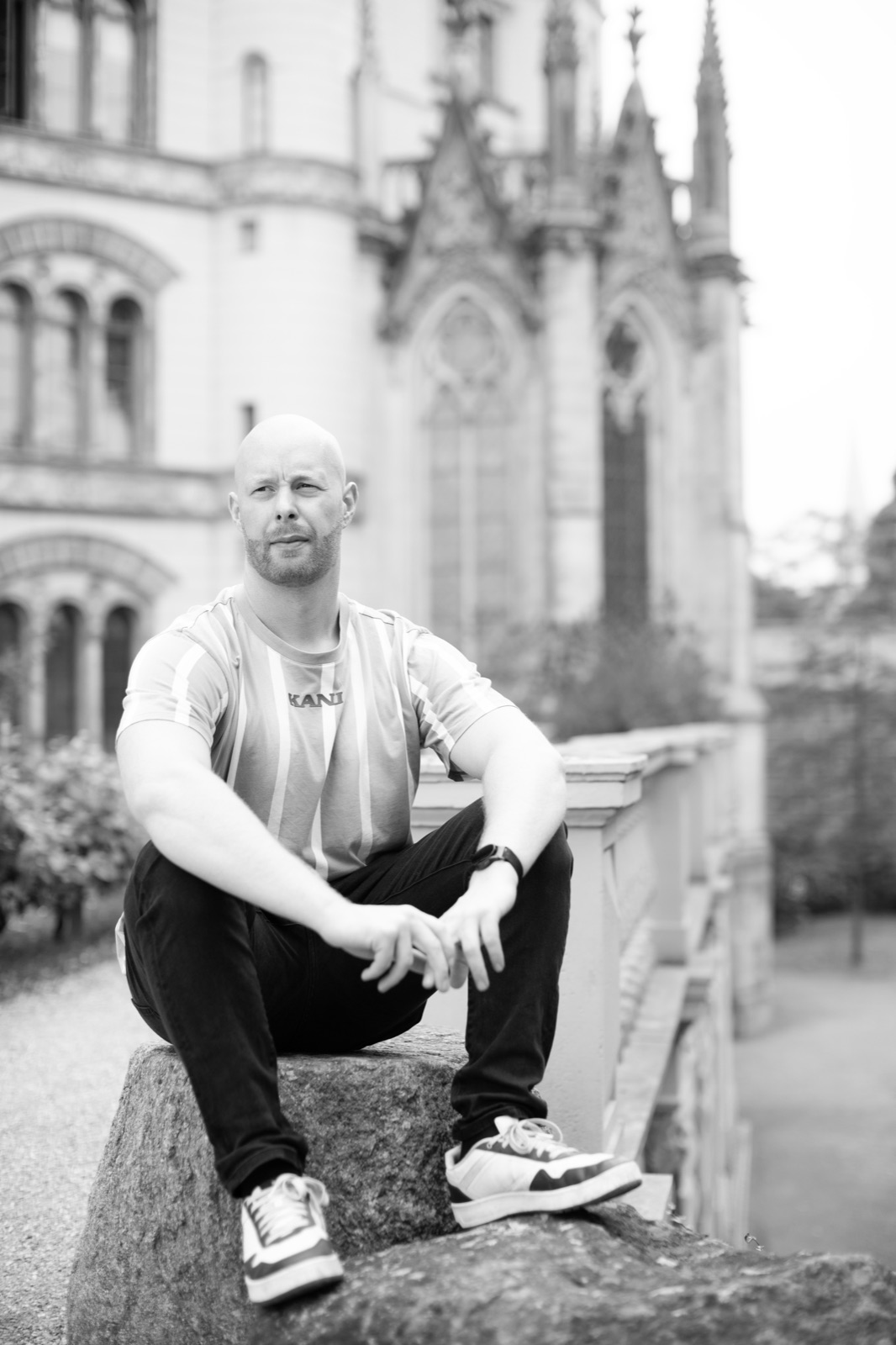 Mann sitzt auf einem Findling vor der Fassade des Schweriner Schlosses, schwarzweiß