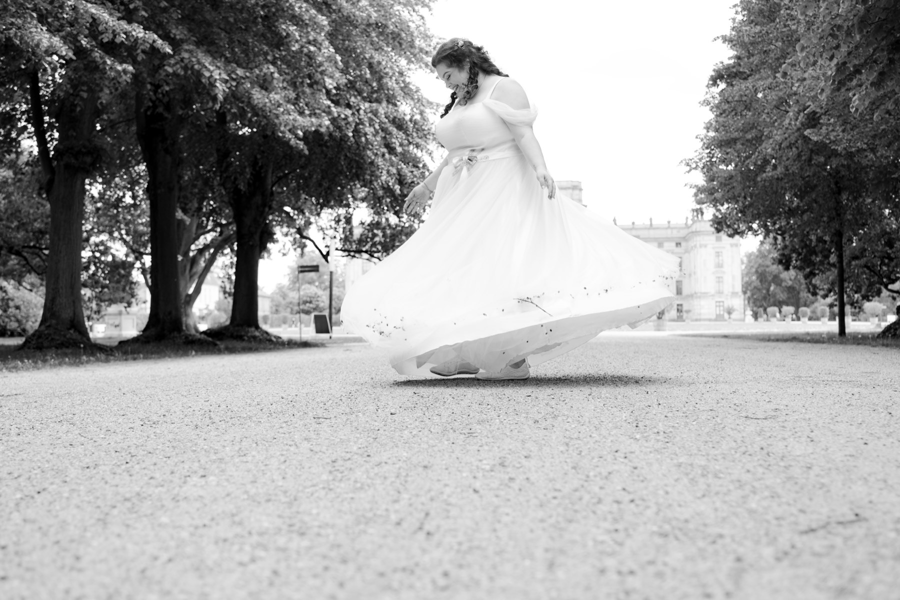 Braut dreht sich mit wehendem weißen Kleid auf einer Allee in Grabow, im Hintergrund das Schloss, schwarzweiß